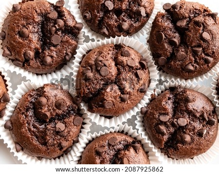 Chocolate muffins in white baking paper cup from above. Close-up of brown cupcakes with chocolate drops. Top view, flat lay