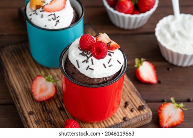 Chocolate Mug Cake With Whipped Cream And Fresh Berries On A Dark Wooden Background. Cupcake Cooked In The Microwave