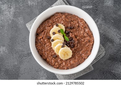Chocolate oatmeal porridge with banana and chocolate chips on top in a white bowl. Healthy breakfast. Copy space