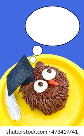 A Chocolate Owl Cupcake Wears A Graduation Cap Decoration And Looks Up At A Thought Bubble. Background Is A Solid Royal Blue Color.