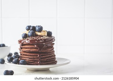 Chocolate pancakes with chocolate cream and blueberries, white kitchen table background, copy space.
