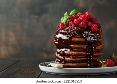 Chocolate Pancakes. Pancakes with fresh raspberry with chocolate glaze or toppings in gray bowl on old wooden table background. Homemade classic american pancakes. Page for magazine concept. - Shutterstock ID 2221018513