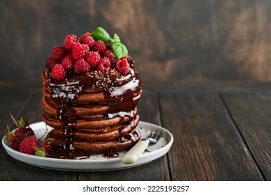 Chocolate Pancakes. Pancakes with fresh raspberry with chocolate glaze or toppings in gray bowl on old wooden table background. Homemade classic american pancakes. Page for magazine concept. - Shutterstock ID 2225195257