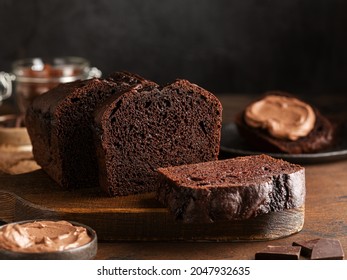 Chocolate pound cake. Loaf of cake sliced into pieces and served with chocolate ganache cream. Brown wooden background. Dark mood. - Shutterstock ID 2047932635