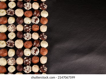 Chocolate pralines, top view of various chocolate pralines isolated on half black leather background. Chocolate candies, white, dark, and milk chocolate concept photo with copy space. 