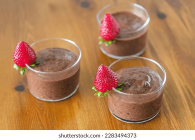 chocolate pudding in glasses decorated with ripe fragrant strawberries on a wooden table - Powered by Shutterstock