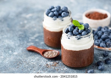 Chocolate pudding and greek yogurt parfait with blueberries in glass jar on blue background. Healthy dessert chia pudding