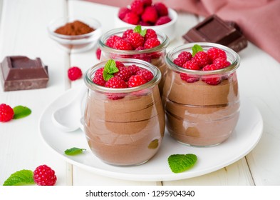 Chocolate Pudding (mousse) With Fresh Raspberries In Glass Jars On A White Wooden Background. 
Dessert On Valentine's Day Or Women's Day.