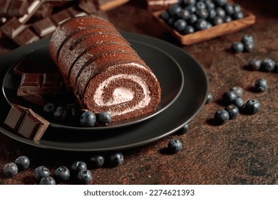 Chocolate roll cake with blueberries and a broken black chocolate bar. - Shutterstock ID 2274621393