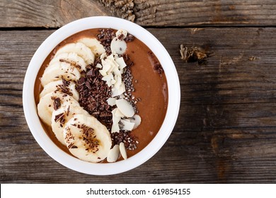 Chocolate smoothie bowl with banana, chia seeds and almond chips on wooden background