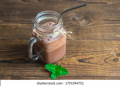 Chocolate Smoothie, Cocktail, Almond Milk And Cream Drink In A Glass Jar With A Reusable Iron Straw And Mint Leaves On A Wooden Background. Place For Text.