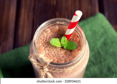 Chocolate smoothie (milkshake) with mint and straw in jar on dark wooden table