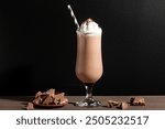 Chocolate smoothie or milkshake and chocolate pieces on black wooden background, copy space. Healthy breakfast protein rich chocolate drink with whipped cream.