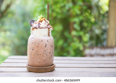 Chocolate smoothie (milkshake) with  straw in jar on wooden table in the garden with copy space