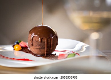 Chocolate sphere cake poured with hot chocolate on white plate in restaurant - Shutterstock ID 2058538958