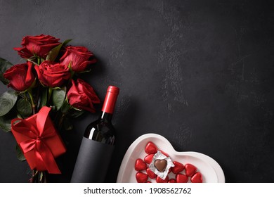 Chocolate sweets, red roses, and red wine with gift on black for Valentine's day. Greeting card with copy space.