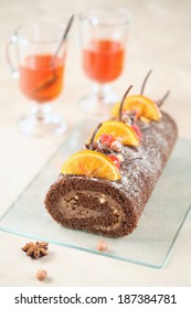 Chocolate Swiss Roll Cake with candied orange slices, cherries and hazelnuts, two cups of fruit tea on a light beige background.