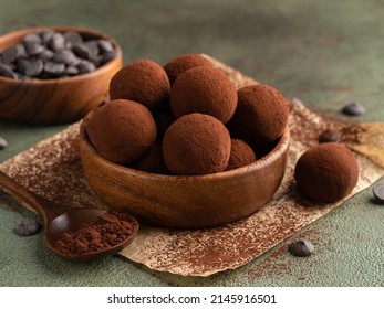 Chocolate truffles covered with cocoa powder in brown wooden bowl with dark chocolate pieces and cocoa powder in wooden spoon. Green background. Closeup view. Delicious homemade dessert. - Powered by Shutterstock