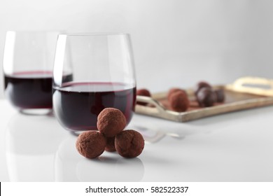 Chocolate truffles and glasses with red wine on white table