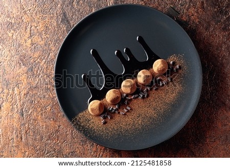 Chocolate truffles on a black plate with chocolate sauce. Sweets are sprinkled with cocoa powder. Top view. 