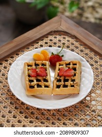 Chocolate Waffel Or Waffle With Strawberry And Orange Fruits For Topping, Serving In White Plate On Rattan Wicker Table.