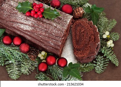 Chocolate yule log cake with red bauble decorations, holly, ivy, mistletoe and snow covered fir over brown handmade lokta paper background. - Shutterstock ID 213621034