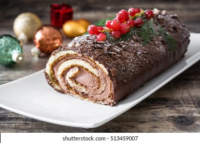 Chocolate yule log cake with red currant on wooden background
