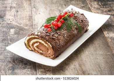 Chocolate yule log christmas cake with red currant on wooden background
