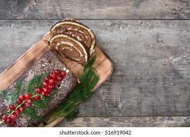 Chocolate yule log christmas cake with red currant on wooden background.copyspace
