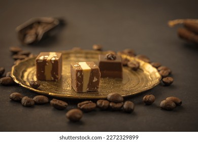 Chocolates treats, pralines, nuts, coffee beans on vintage metallic plate on dark background, copy space 