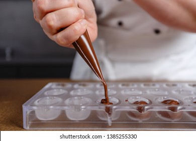 Chocolatier pours chocolate into molds. Chef in white apron using pastry bag filling hot melt chocolate into silicone mold. Concept for making homemade chocolate dessert in modern clean kitchen. - Powered by Shutterstock