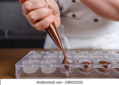 Chocolatier pours chocolate into molds. Chef in white apron using pastry bag filling hot melt chocolate into silicone mold. Concept for making homemade chocolate dessert in modern clean kitchen. - Powered by Shutterstock