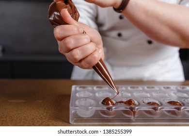 Chocolatier pours chocolate into molds. Chef in white apron using pastry bag filling hot melt chocolate into silicone mold. Concept for making homemade chocolate dessert in modern clean kitchen. - Powered by Shutterstock