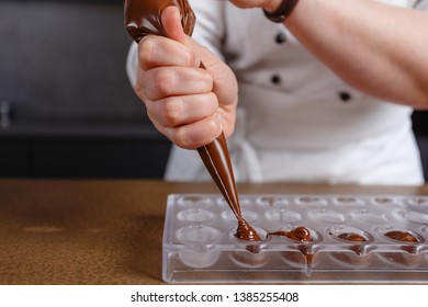 Chocolatier pours chocolate into molds. Chef in white apron using pastry bag filling hot melt chocolate into silicone mold. Concept for making homemade chocolate dessert in modern clean kitchen. - Powered by Shutterstock