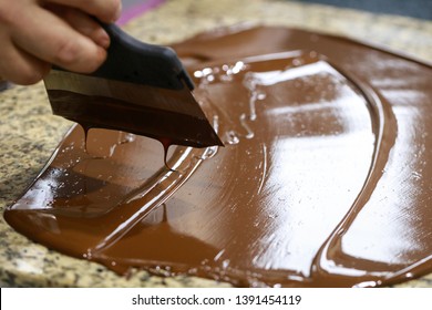 Chocolatier with a spatula is stirring the tempered liquid chocolate on a granite table