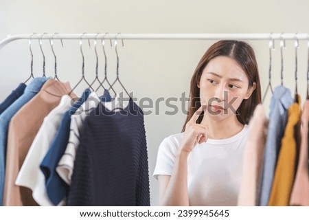 Choice of clothes, girl try on apparel, worry choosing dress, Nothing to wear. Attractive asian young woman, outfit on hanger, wardrobe in room closet at home. Deciding blouse what to put on which one