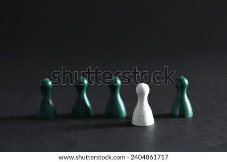 Choice concept. White pawn and green ones on dark table