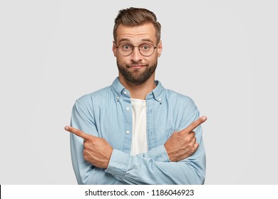 Choice in not made. Hesitant and clueless man crosses hands over chest, indicates with index fingers in different sides or directions, cant make choice between two items, poses over white background