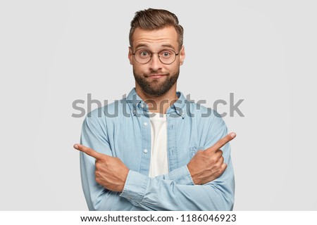 Choice in not made. Hesitant and clueless man crosses hands over chest, indicates with index fingers in different sides or directions, cant make choice between two items, poses over white background