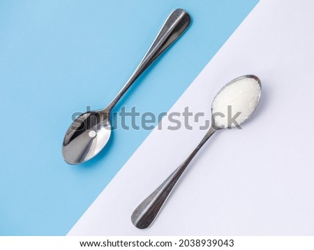 Choice of Sweetener in tablets or regular sugar. Alternative to sugar for diabetics. Sugar-replacement tablet and sugar in tea spoons lying in opposite diagonal directions on blue white background.