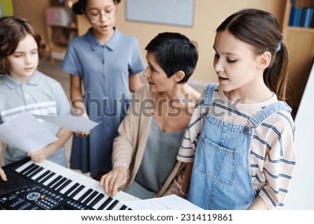 Choir of children singing songs in music class while teacher playing piano and singing together with them