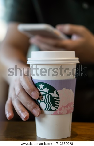 Chon Buri,Thailand/Chon Buri March 11, 2020 :Side\
view of Hot coffee cup with new collection  for Cup sleeve sakura\
flower from starbuck ,Thailand. A man using cellphone and carring a\
coffee cup.