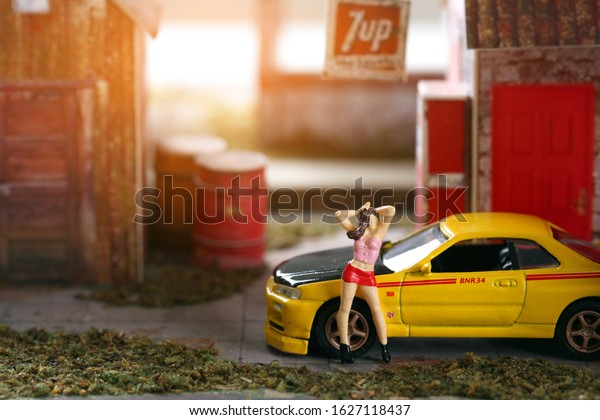 CHONBURI, THAILAND, JANUARY 25, 2020 : Miniature\
people - woman standing poses the back is a yellow toy car, diorama\
style