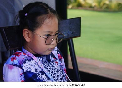 CHONBURI, THAILAND – MARCH 27, 2022: Little Asian Girl Sitting On A Chair To Looking Something For Waiting To Eating The Food In The House In Chonburi Province.