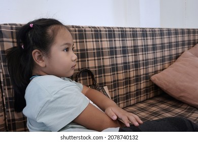 CHONBURI, THAILAND – NOVEMBER 21, 2021: Little Asian Girl Sitting On A Sofa To Looking Something For Waiting To Eating The Food In The House In Chonburi Province.