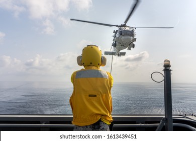 CHONBURI,THAILAND - DECEMBER 24, 2019: Helicopter Deck Officer Gives Hand Signal To Sikorsky S-70 Sea Hawk Helicopter Hovering Above Heli Deck Of Navy Ship To Perform Hot Refueling While Flying At Sea