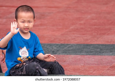 Chongqing, China - May 9, 2010: Central Peoples Square. Closeup Of Young Boy In Blue Shirt Waving Hand. Faded Red Tile Background.