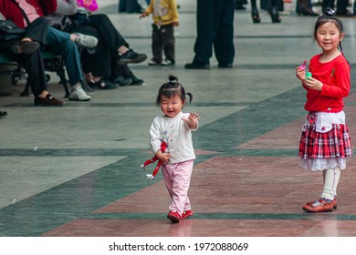 Chongqing, China - May 9, 2010: Central Peoples Square. Toddler Girl Smiling And Waving With Little Girl Blowing Soap Bubbles.