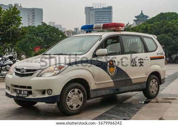 Chongqing, China - May 9, 2010: Downtown. Closeup of\
white parket Police car with green foliage in back and parts of\
tall buildings in silver\
sky.