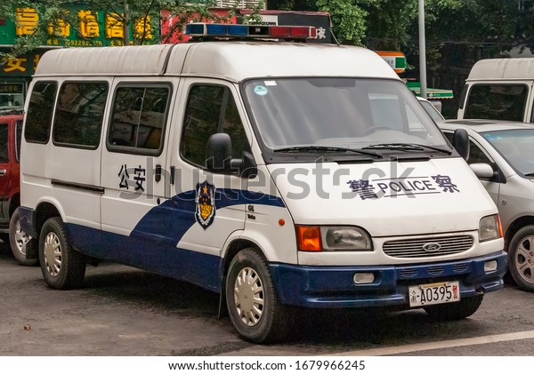 Chongqing, China - May 9, 2010:\
Downtown. Closeup of white parket Police van with green foliage in\
back. parts of other cars and yellow mandarin symbols on\
green.